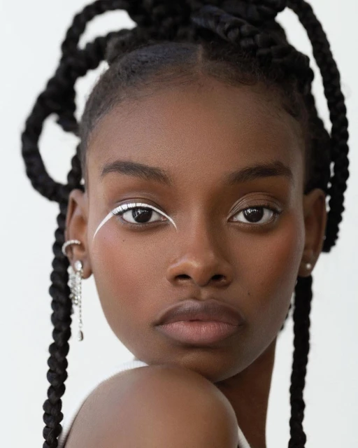 Close-up portrait of a Black woman with stylish eye makeup and braided hair against a white background in a beauty shot.