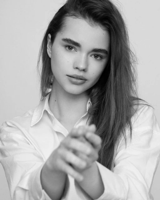 Monochrome portrait of a young adult woman with long hair, wearing a button-down shirt, and posing in front of a light background.
