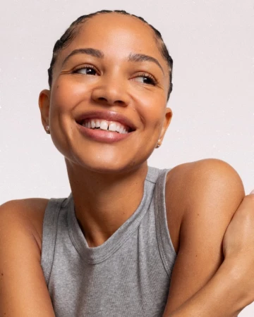 Close-up of a smiling woman with braided hair wearing a gray tank top, set against a white background, showcasing a beauty portrait.