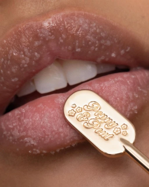 Close-up of woman's lips covered in lip scrub with a gold Peppy & Pout applicator for exfoliation and beauty treatment.