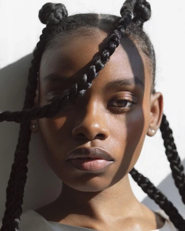 Close-up portrait of a Black woman with braided hair and space buns in bright sunlight by Angela Marklew