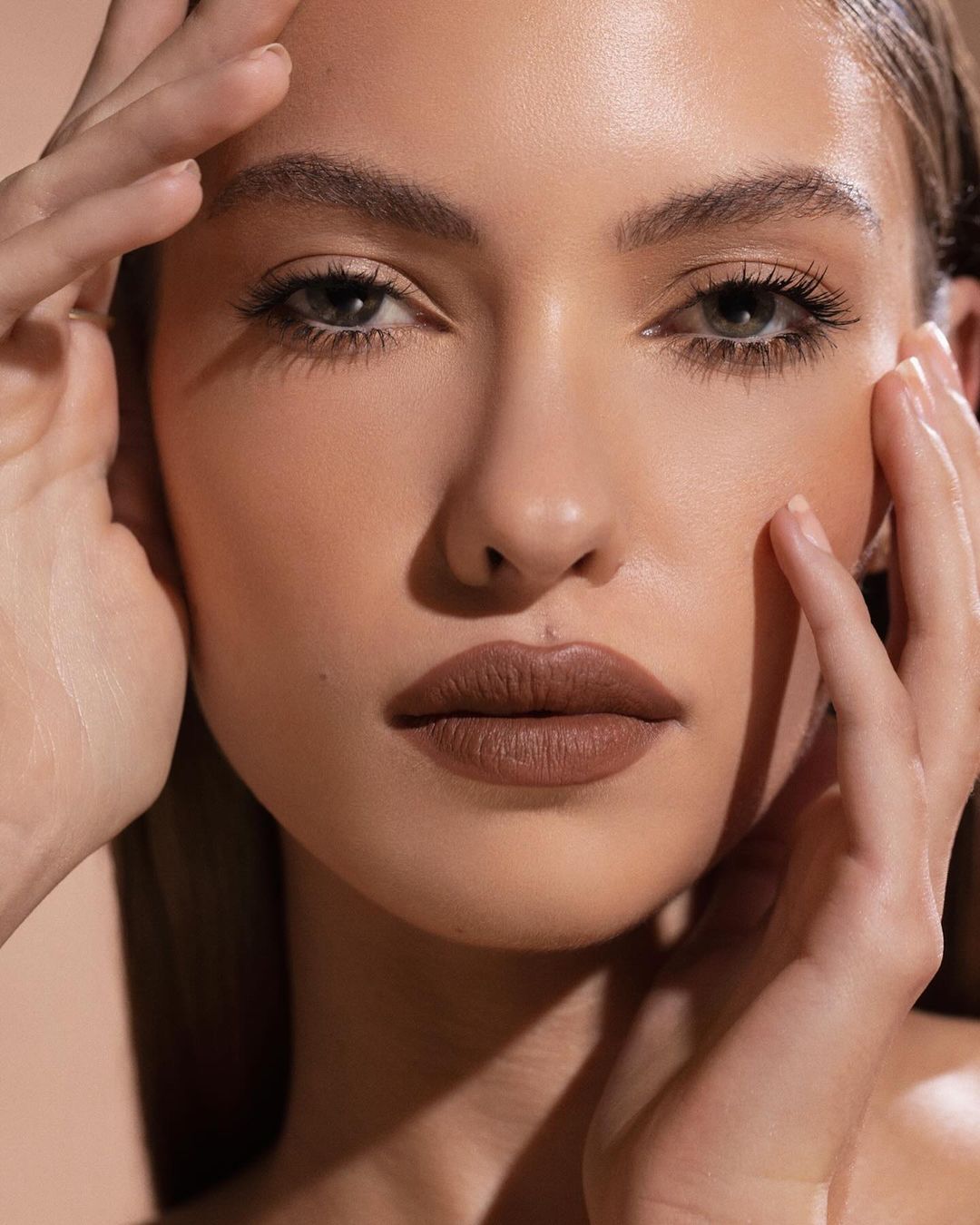 Close-up beauty portrait of a woman with brown matte lipstick posing with hands touching her face by photographer Angela Marklew.