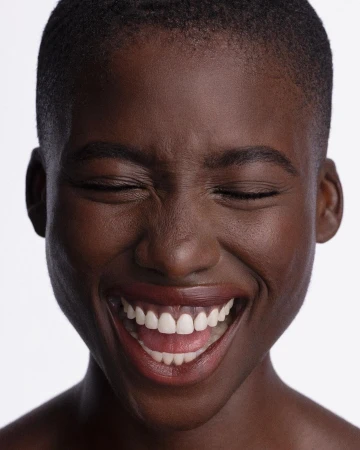 Close-up portrait of a Black woman with short hair laughing with closed eyes by Angela Marklew