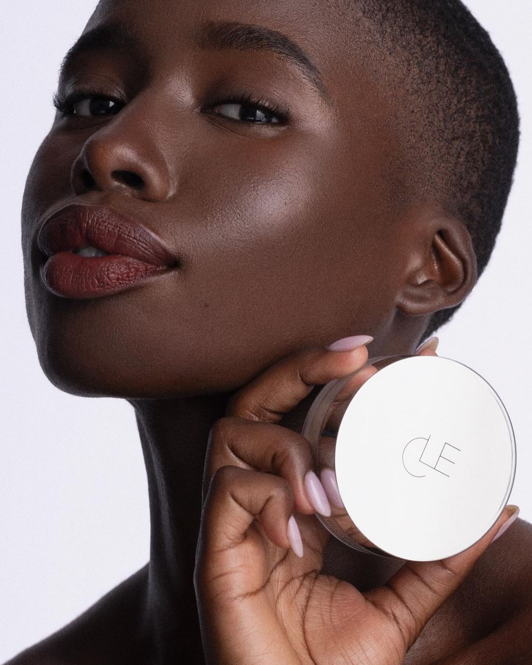 Close-up of an African-American woman with flawless skin holding a CLE beauty product. Focus on beauty, skincare, and product.