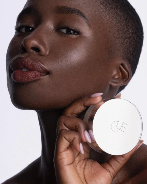 Close-up of an African-American woman with flawless skin holding a CLE beauty product. Focus on beauty, skincare, and product.