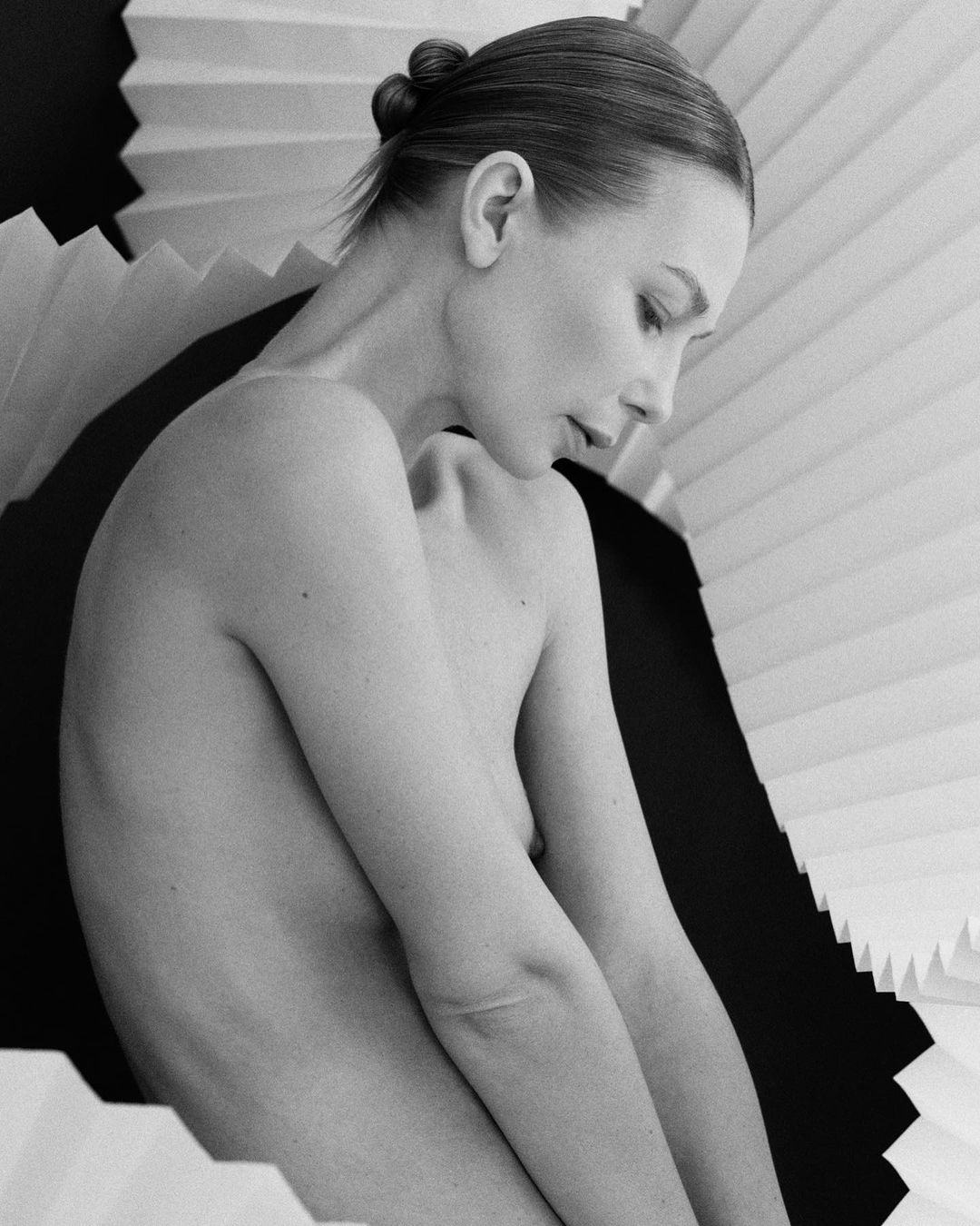 Black and white portrait of a woman with folded paper accentuating her profile, showcasing her face and bare shoulders.
