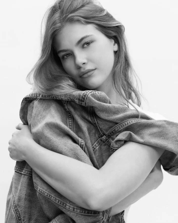 Monochrome portrait of a woman embracing herself while wearing a denim jacket against a white background