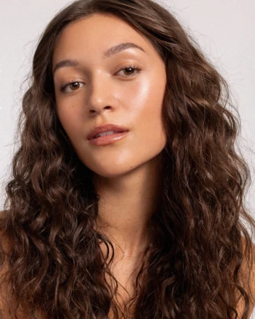 Close up portrait of a young woman with long curly brown hair and glowing skin by photographer Angela Marklew.