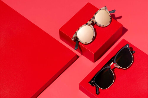 Two pairs of sunglasses on red platforms, one tortoiseshell and one black frame, arranged on a two-tone red backdrop for product photography.