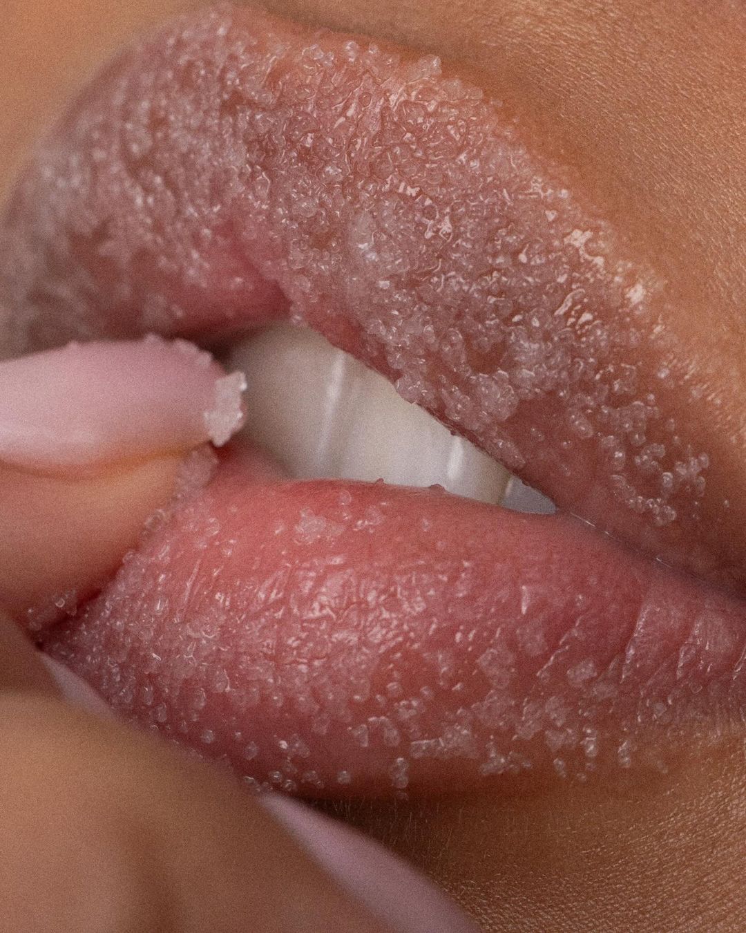 Close-up studio shot of a woman's lips covered with crystal-like particles and the fingers of the same hand holding the lip.
