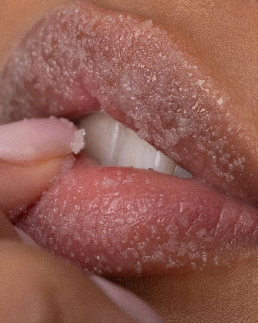 Close-up studio shot of a woman's lips covered with crystal-like particles and the fingers of the same hand holding the lip.