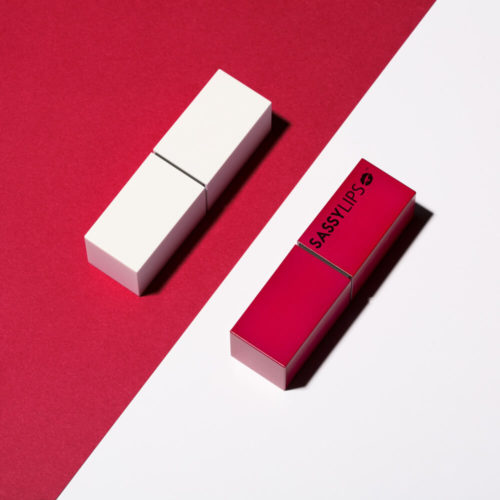 Two lipstick tubes, one white and one red, are presented on a split red and white backdrop, creating a modern, minimalist beauty product shot.