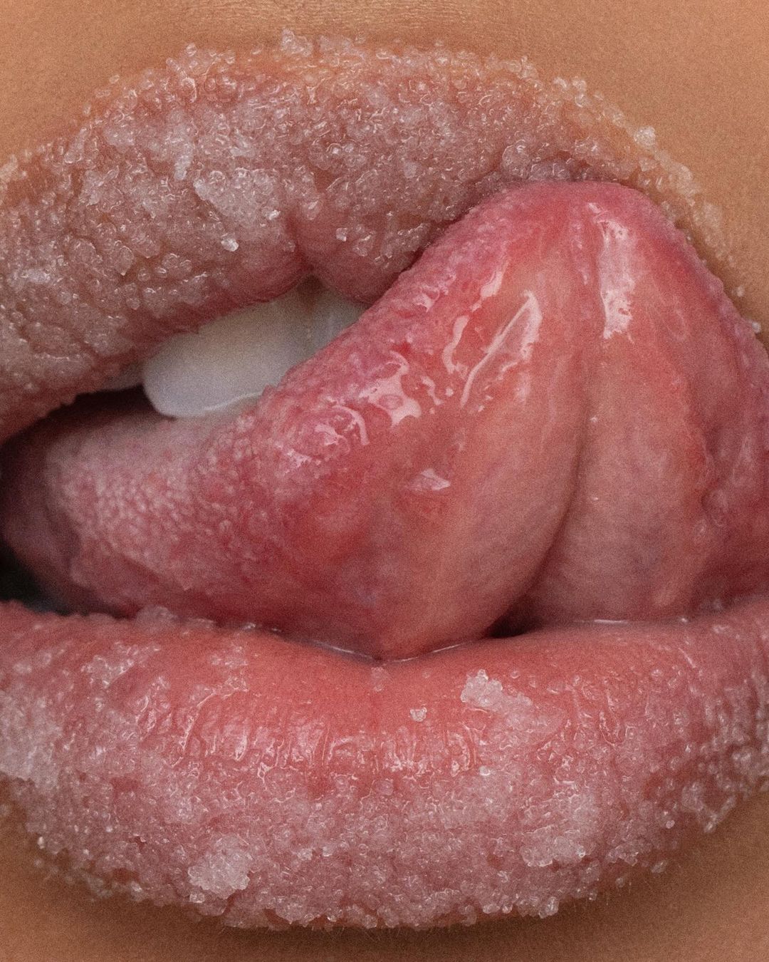 Macro photograph of open human mouth, lips covered in sugar, and tongue sticking out with a glossy, textured appearance.