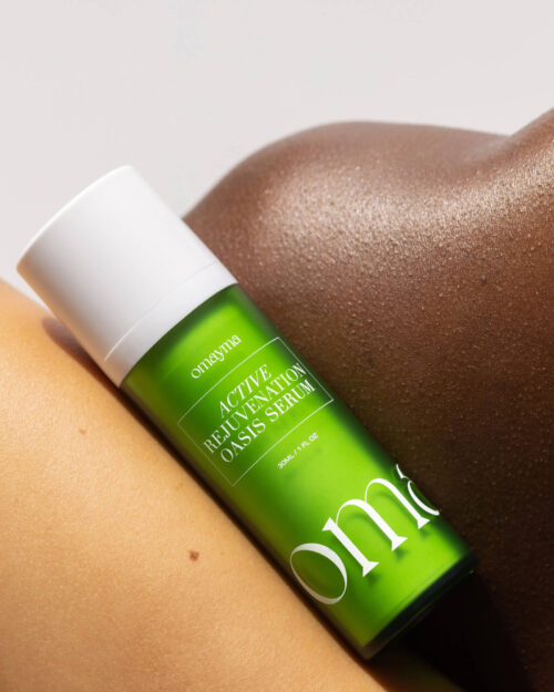 Omayma Active Rejuvenation Oasis Serum bottle with a white cap rests against skin, in a product shot with bright studio lighting.
