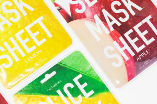 Several sheet face masks are displayed, featuring different fruit extracts such as lemon and apple, on a white background.