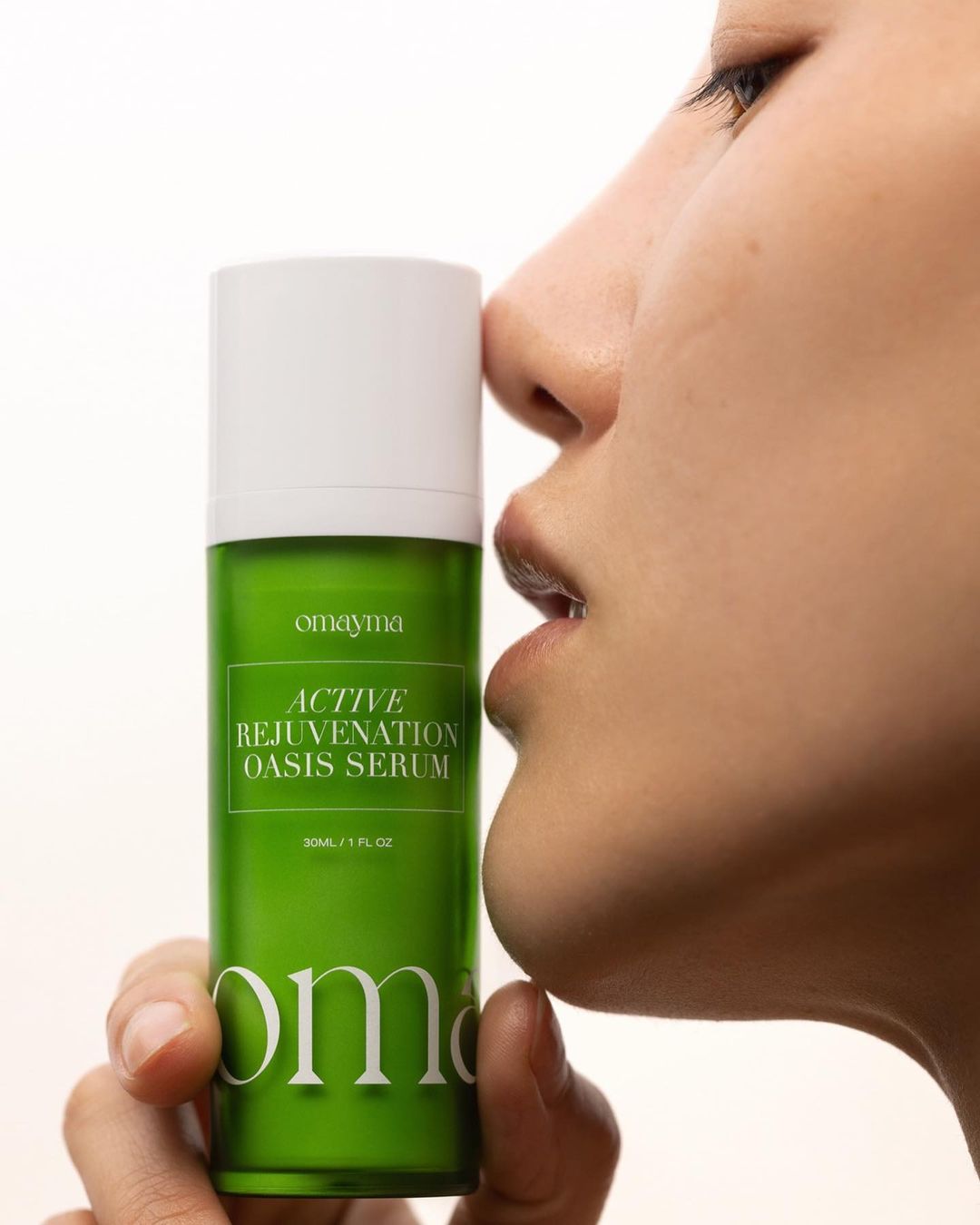 Close-up shot of a woman holding Omayma Active Rejuvenation Oasis Serum, highlighting beauty, skincare, and the product's green packaging.
