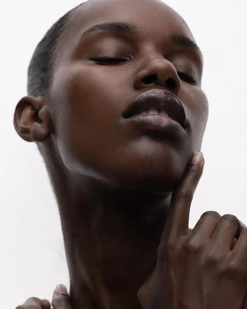 Close-up portrait of a Black woman with closed eyes and her hand touching her chin against a plain white background
