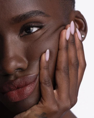 Close-up portrait of a Black woman with almond-shaped light pink manicured nails touching her face