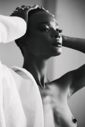 Black-and-white portrait of a woman with her hands in her hair wearing a white garment by Angela Marklew