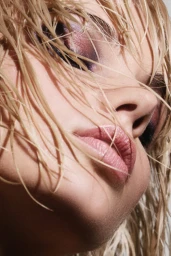 Extreme close-up portrait of a woman with wet blonde hair covering her face and glossy pink lips