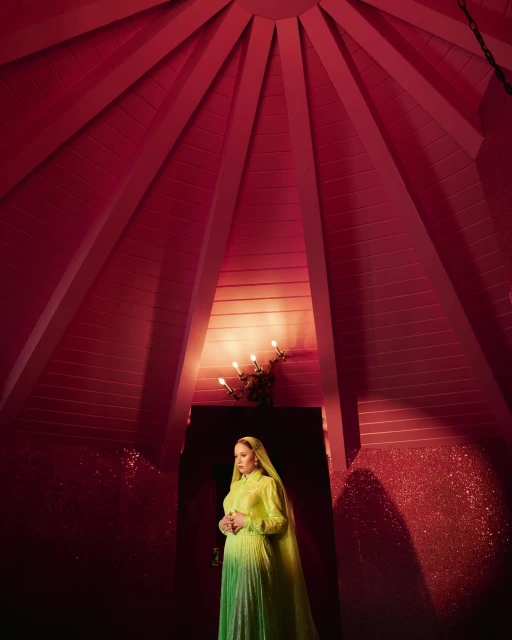 Portrait of a pregnant woman in a green dress standing indoors beneath a unique red ceiling with sconce lighting, in a serene pose.