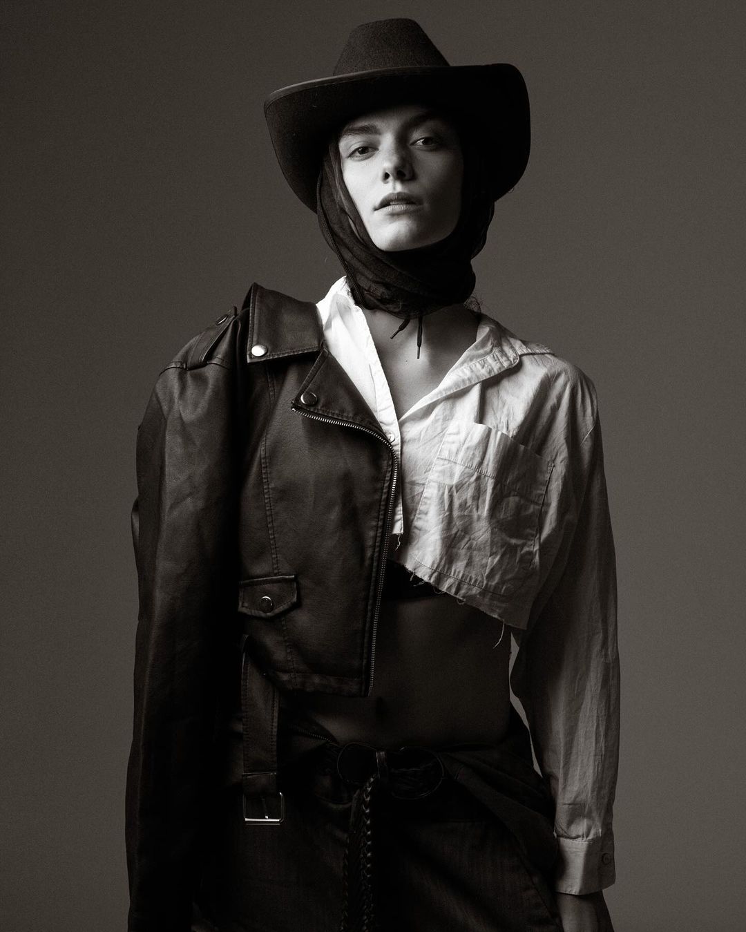 Monochrome portrait of a model in a cowboy hat, white shirt, and leather jacket draped over one shoulder