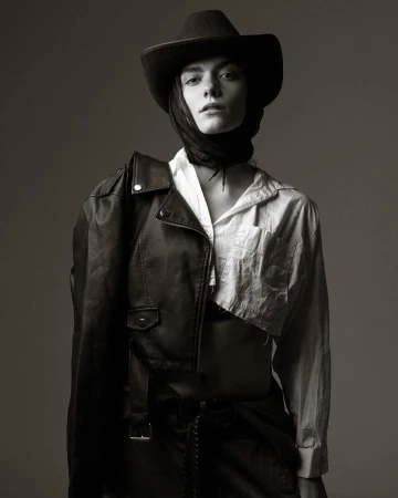 Monochrome portrait of a model in a cowboy hat, white shirt, and leather jacket draped over one shoulder