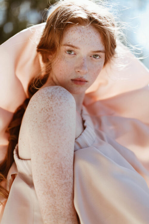Portrait of a freckled redheaded woman in a pale pink ruffled garment outdoors in natural sunlight