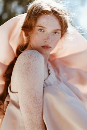 Portrait of a freckled redheaded woman in a pale pink ruffled garment outdoors in natural sunlight