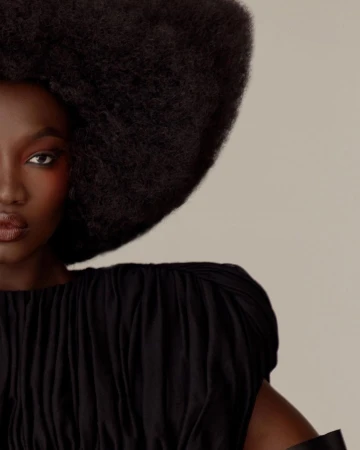 Close-up portrait of a Black woman with a large afro hairstyle and dark top against a neutral background.