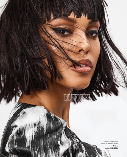 Close-up of an African American female model with short black hair, wearing a patterned black and white top, in a studio setting.