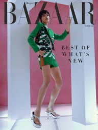 Model in green patterned blazer and shorts posing between white architectural pillars against pink backdrop