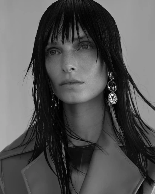 Black and white portrait of a woman with dark, wet hair and wearing a trench coat and jeweled earrings. Fashion and beauty concept.