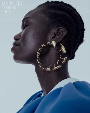 Close-up fashion shot of an African woman with braided hair wearing a gold earring and a blue dress on a light background.