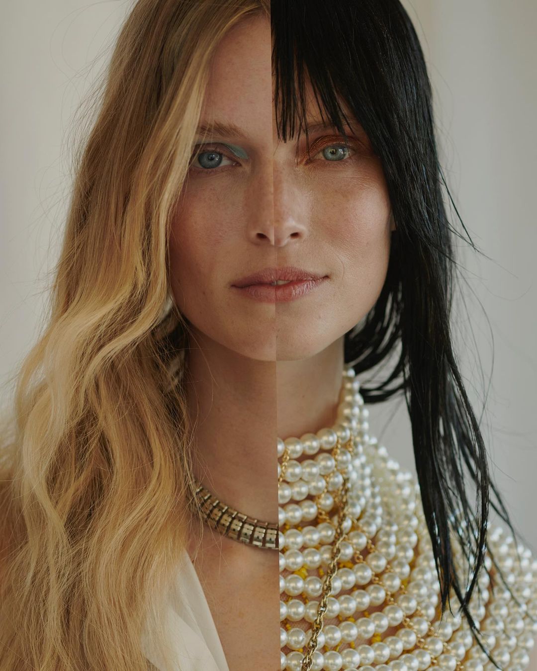 Fashion portrait of a fair-skinned woman with heterochromia; half blonde wavy hair, half black straight hair; wearing pearl necklaces.
