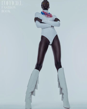 Full-length studio shot of a dark-skinned woman in a white bodysuit and heeled boots, posing confidently against a plain background.