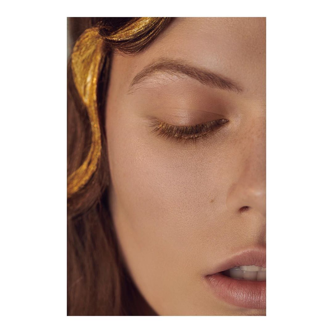 Close-up studio shot of a woman's face with golden hair accents, showcasing beauty and makeup details in a naturally lit setting.