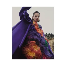 Model wearing a purple coat with colorful feathered texture against an outdoor landscape by photographer Eva Schwank
