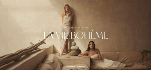 Two adult women pose in a bright, minimalist interior space with neutral tones, promoting a fashion collection with lifestyle appeal.