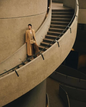 Model wearing a long beige coat standing on a curved concrete staircase by Justin Wilczynski.