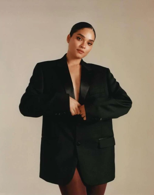 Elegant adult woman wearing a black blazer in a studio setting, posing for a fashion-forward portrait with a neutral background.