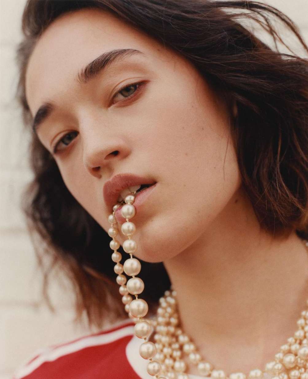 Close-up portrait of a young woman with brunette hair, fair skin, wearing pearls in a photo studio with a neutral background.