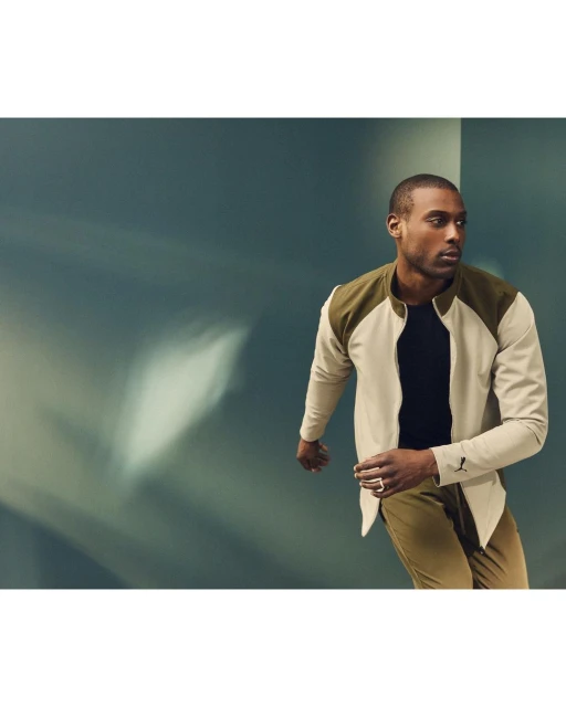 Portrait of an adult Black male wearing a stylish two-tone jacket and khaki pants, posing in a photo studio with turquoise wall.