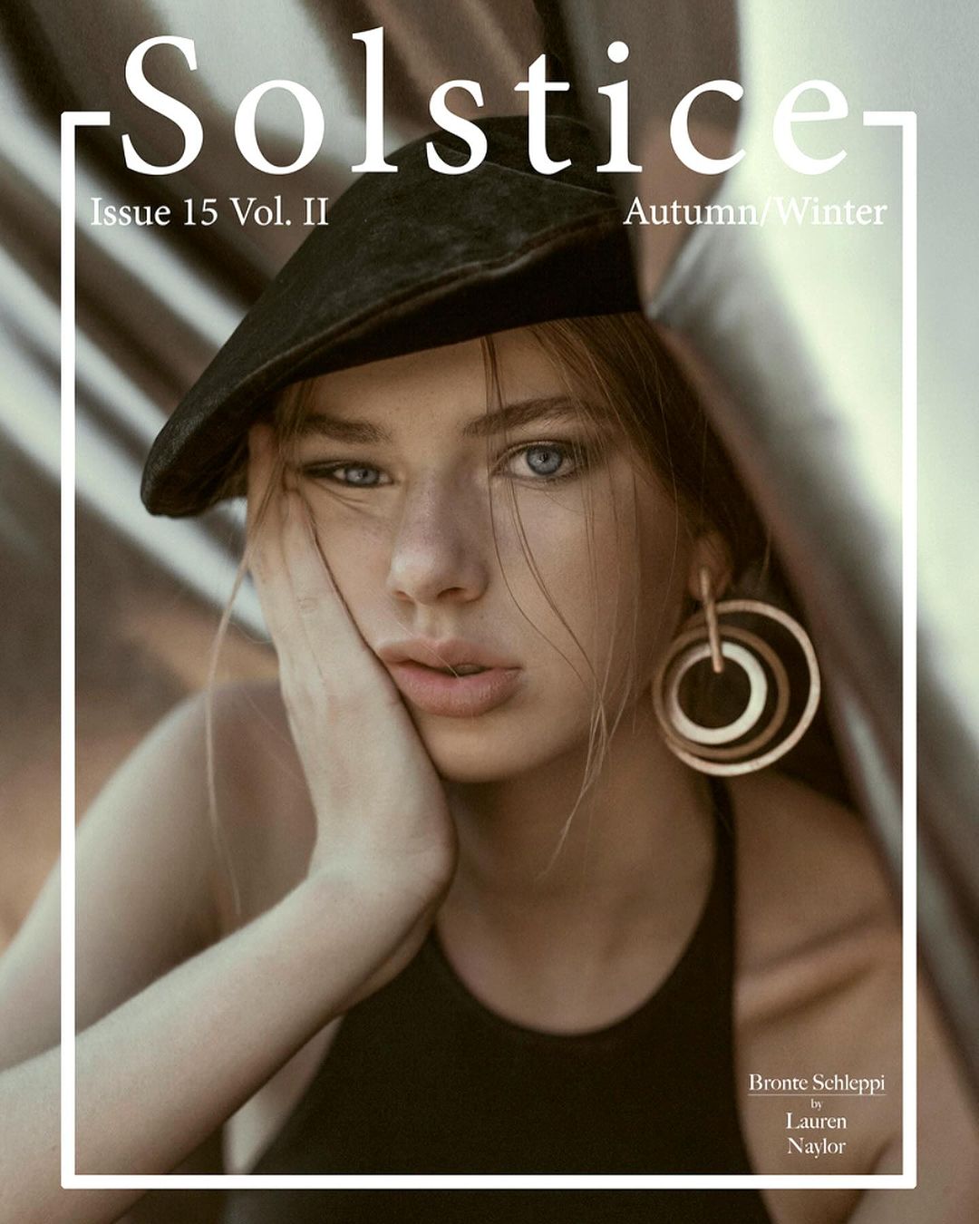 Close-up fashion portrait of a young woman wearing a dark cap and large hoop earrings, photographed by Lauren Naylor.