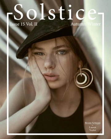 Close-up fashion portrait of a young woman wearing a dark cap and large hoop earrings, photographed by Lauren Naylor.