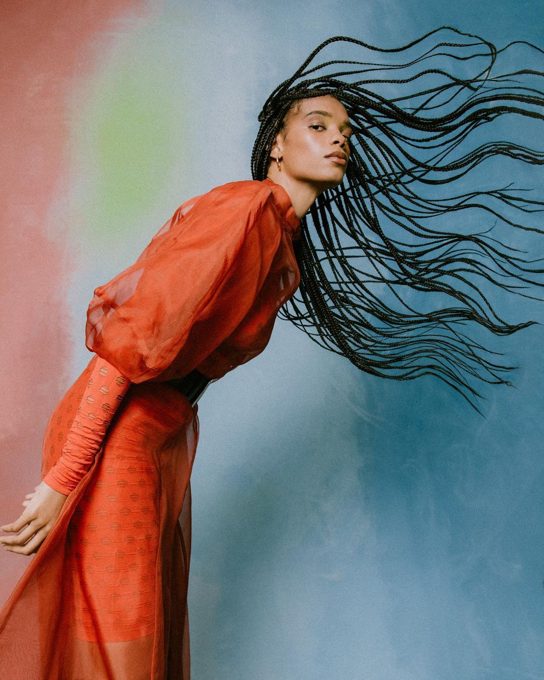 Portrait of a woman in an orange dress and long braids, with a black belt against a colorful background. Fashion and beauty shot.