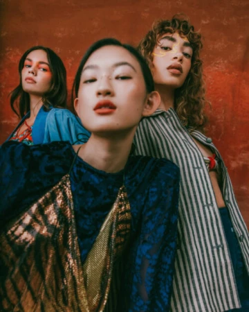Three female models posing against a rustic textured red background in varied patterned apparel.