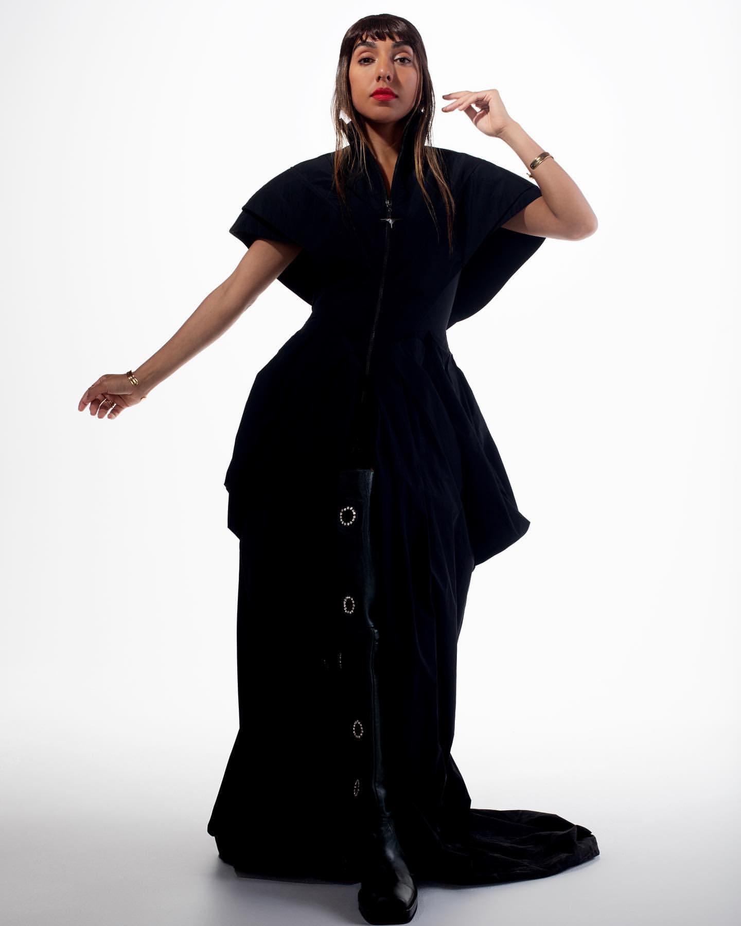 Model in black structured dress and tall boots posing against a bright white background