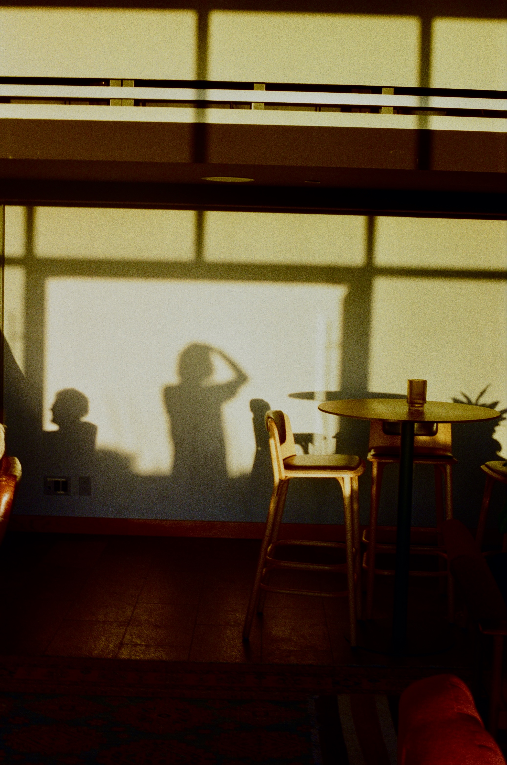 Interior shot with shadows of two people on wall, table with chairs, and dark hardwood floor, creating a moody, warm atmosphere.
