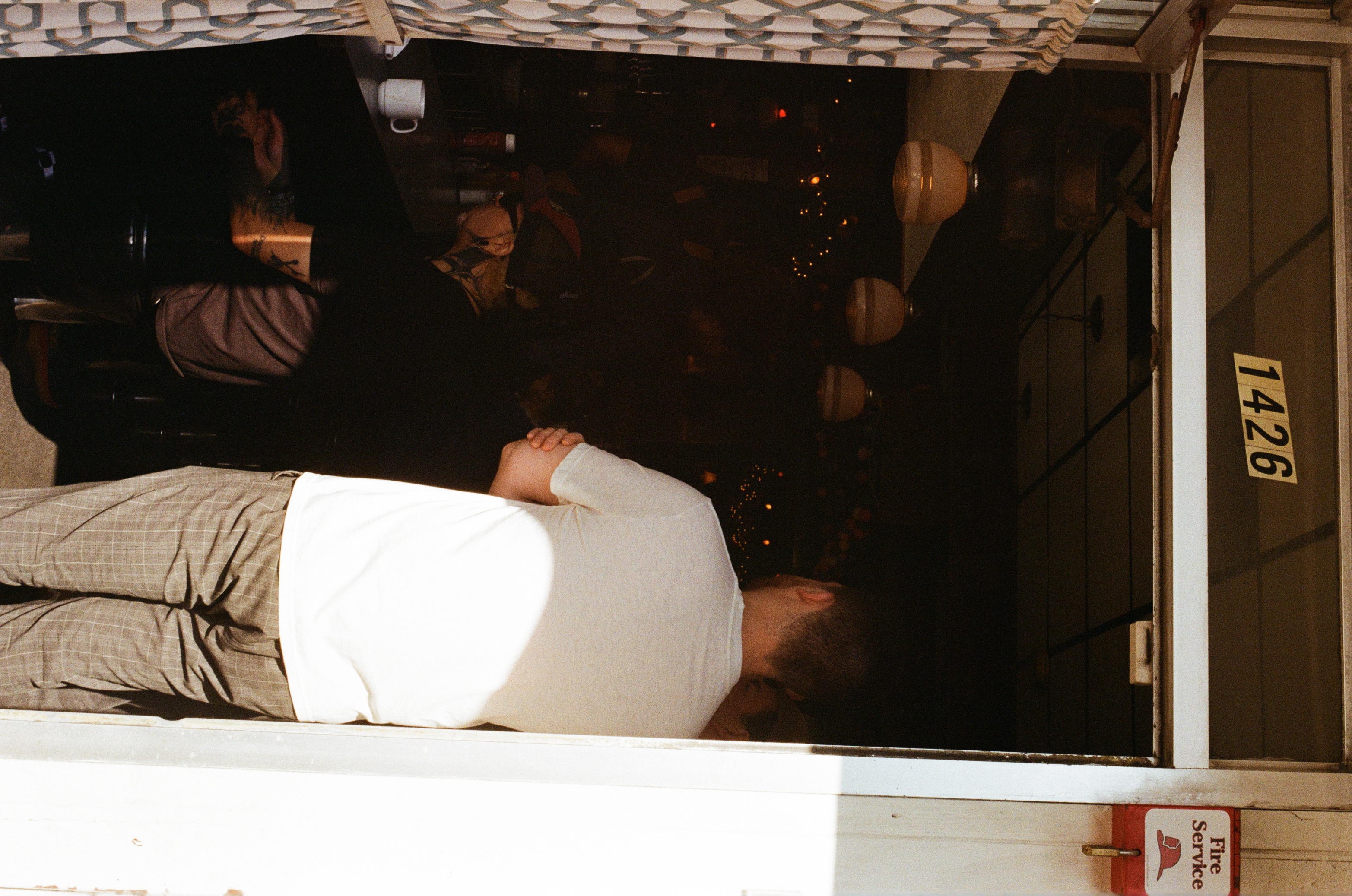Adult male entering dimly lit restaurant through open doorway, patron sitting at bar, overhead lighting visible inside.